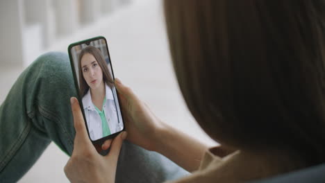 Woman-checks-possible-symptoms-with-professional-physician-using-online-video-chat.-Young-girl-sick-at-home-using-smartphone-to-talk-to-her-doctor-via-video-conference-medical-app.